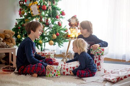 Happy children, boys, opening presents on christmas day, dressed in pajamasの写真素材
