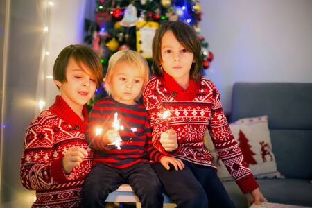 Waist up portrait of happy children celebrating New Year together and lighting sparklers at homeの写真素材