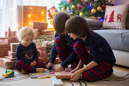 Happy children, boys, opening presents on christmas day, dressed in pajamasの写真素材