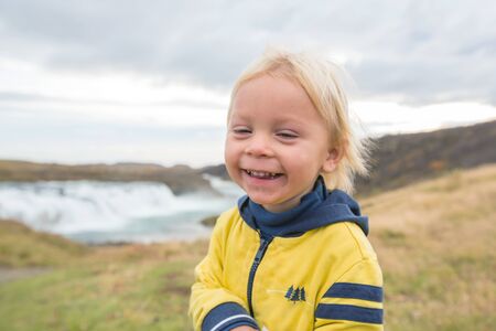 Portrait of a smiling baby boy near smaller waterfall around Gullfoss, Iceland autumntime