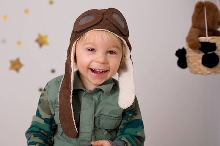 Sweet toddler boy, playing with airplane and teddy bear, decorated air balloons with toys behind himの写真素材