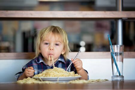 Little baby boy, toddler child, eating spaghetti for lunch and making feeding teddy bear friend, pot with spaghetti and tomatoes on the tableの写真素材