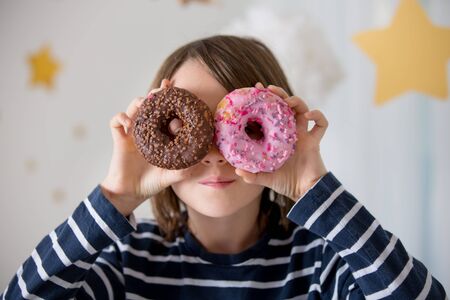 Cute sweet blonde child, playing and eating donuts at homeの写真素材