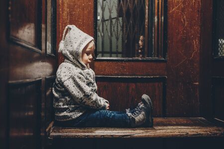 Sweet toddler blonde boy, sitting in an old wooden elevator or lift with gratingの写真素材