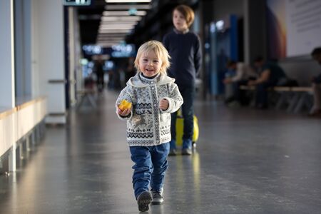 Blonde toddler boy with family, traveling with airplane, running at the airport with suitcaseの写真素材
