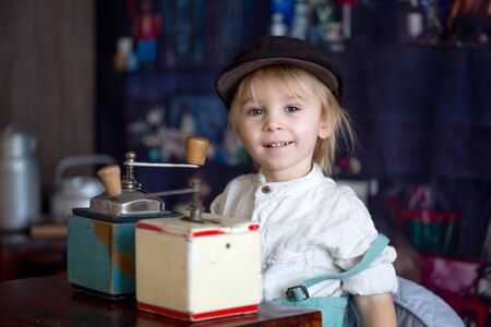 Little toddler boy, playing with mill at home, sitting on vintage table with retro toys around himの写真素材