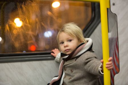 Sweet toddler boy,riding in train on a cold winter night, looking at camera