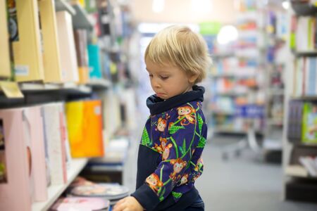 Adorable little boy, sitting in a book store and read bookの写真素材