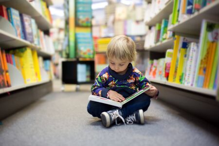 Adorable little boy, sitting in a book store and read book