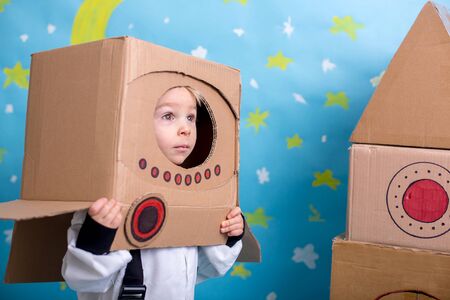 Sweet toddler boy, dressed as an astronaut, playing at home with cardboard rocket and handmade helmet from boxの写真素材