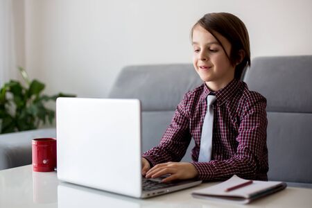 School child, sitting at the table with laptop, writing school tasks while homeschooling, while school closed due to Coronavirusの写真素材