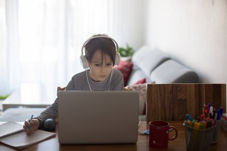 School child, sitting at the table with laptop, writing school tasks while homeschooling, while...