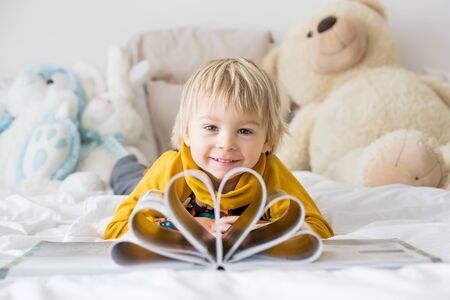 Beautiful child, toddler boy, reading book and playing with it, creative knowledge shot with book and lettersの写真素材