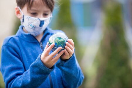 School child, holding small globe, looking sad at the world ruding Covid 19 pandemic, virus that...