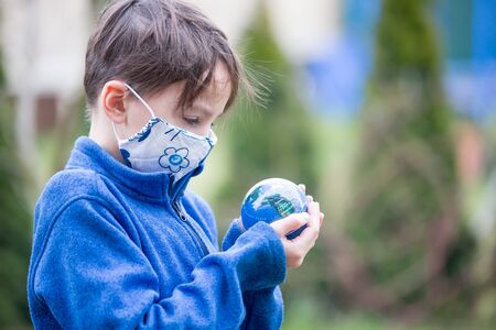 School child, holding small globe, looking sad at the world ruding Covid 19 pandemic, virus that spread worldwideの写真素材