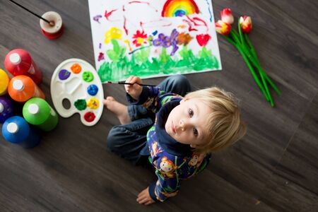 Sweet toddler blond child, boy, painting with colors, little chicks walking around him, making funny prints on his paperの写真素材