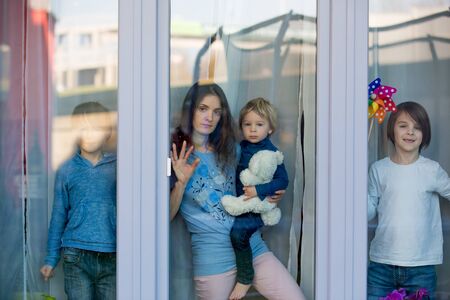 Family, standing behind the window, at home, quarantine due to coronavirusの写真素材