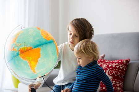Little children, brothers, looking at illuminated globe, exploring the world, learningの写真素材