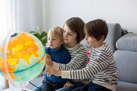 Little children, brothers, looking at illuminated globe, exploring the world, learning