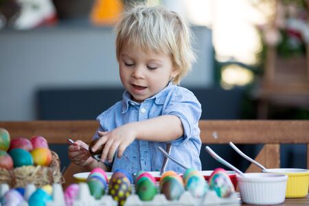 Sweet children, brothers, coloring and paiting eggs for Easter in garden, outdoors at home in backyardの写真素材