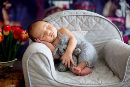 Little newborn baby boy, sleeping in little cozy baby armchair with little knitted toy, comfortably asleepの写真素材