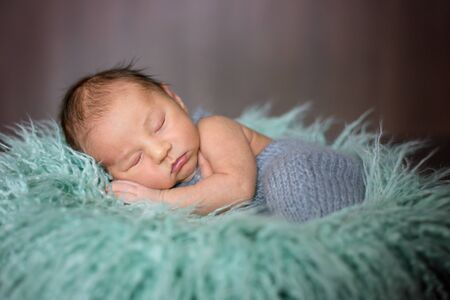Cute little newborn baby boy, sleeping in basket with colorful wrapの写真素材