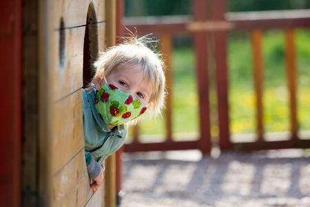 Blonde little toddler child inwearing protective mask, playing on the playground, spring sunny dayの写真素材