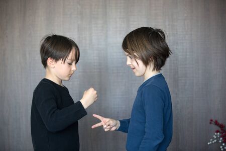 Two children, boy brothers, playing rock scissors paper game in garden