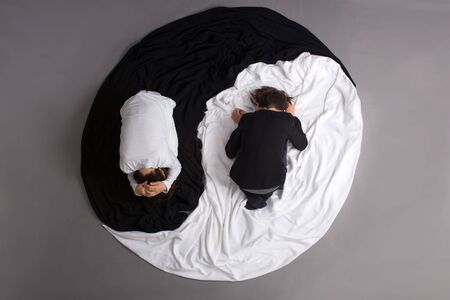 Two children, dressed in black and white, lying on the floor in Yin -Yang circle, isolated image