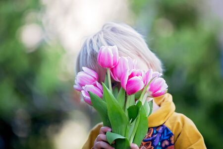 Child, boy holding pink tulips , hiding behind them, mothers day gift conceptの写真素材