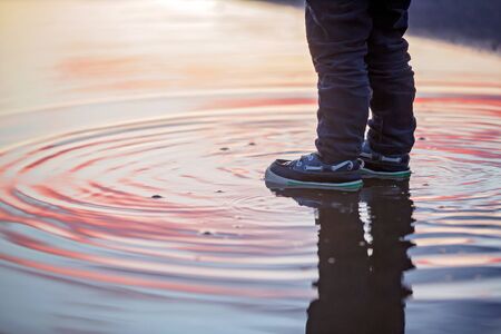 Sweet toddler child, cute boy with red raincoat, playing in puddle on sunset
