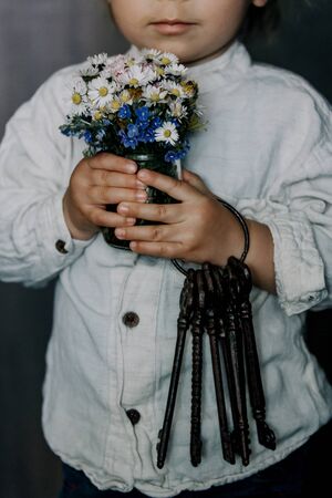 Toddler child, holding old vintage keys and bouquet of wild flowers in little vase