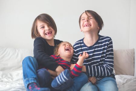 Three children, boy brothers, laughing in bed, gigling and ticklingの写真素材