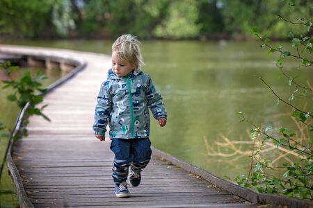 Child, boy, sitting or running on a wooden bridge over lake on a spring day