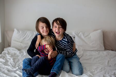 Three children, boy brothers, laughing in bed, gigling and tickling
