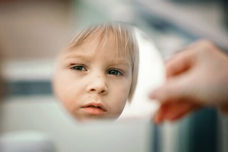 Reflection of a cute little toddler boy, child, looking in mirror, outdoorsの写真素材
