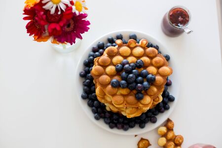 Sweet toddler child, boy, eating bubble waffles with fruits at home for breakfast, flowers on the tableの写真素材