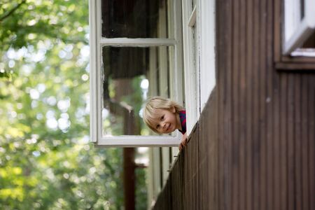Cute toddler boy, looking out of the window of chalet in the woods, springtimeの写真素材