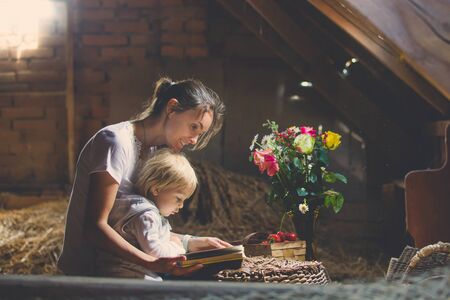 Little toddler blond boy, reading a book in the attic, nice atmosphere, flowers and strawberries next to himの写真素材
