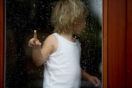 Sad child behind the window on a rainy dayの写真素材