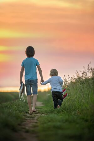 Happy children, boy brothers, holding pair of sneakers in hands, walking on a rural path, barefeetの写真素材