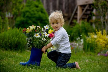 Child holding rubber boots with beautiful flowers in gardenの写真素材