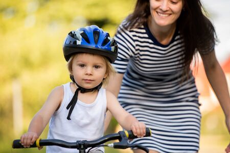 Young mother, helping her son to learn how to ride a bike, holding him and teaching him bikingの写真素材