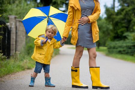 Mother and toddler child, boy, playing in the rain, wearing boots and raincoatsの写真素材