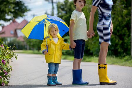 Mother and toddler child, boy, playing in the rain, wearing boots and raincoatsの写真素材