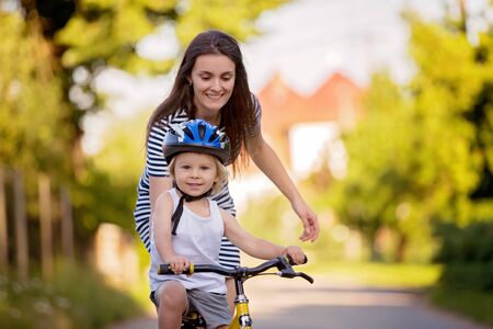 Young mother, helping her son to learn how to ride a bike, holding him and teaching him bikingの写真素材