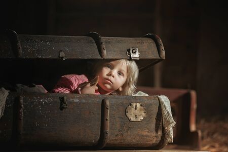 Little child, boy, hiding in old vintage suitcase in the attic, scared not to be foundの写真素材