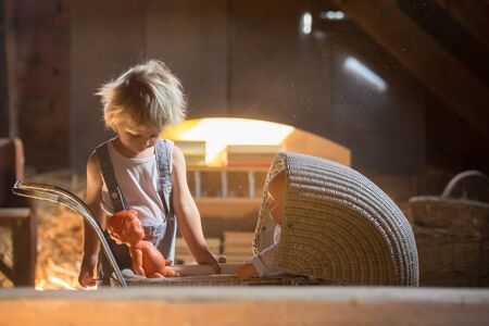 Little toddler boy, playing with doll stroller and baby doll in attic, nice soft lightの写真素材