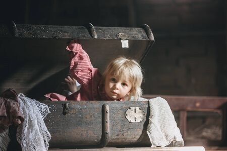 Little child, boy, hiding in old vintage suitcase in the attic, scared not to be foundの写真素材