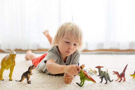 Blond toddler child, playing with dinosaurs at home, nice soft back lightの写真素材